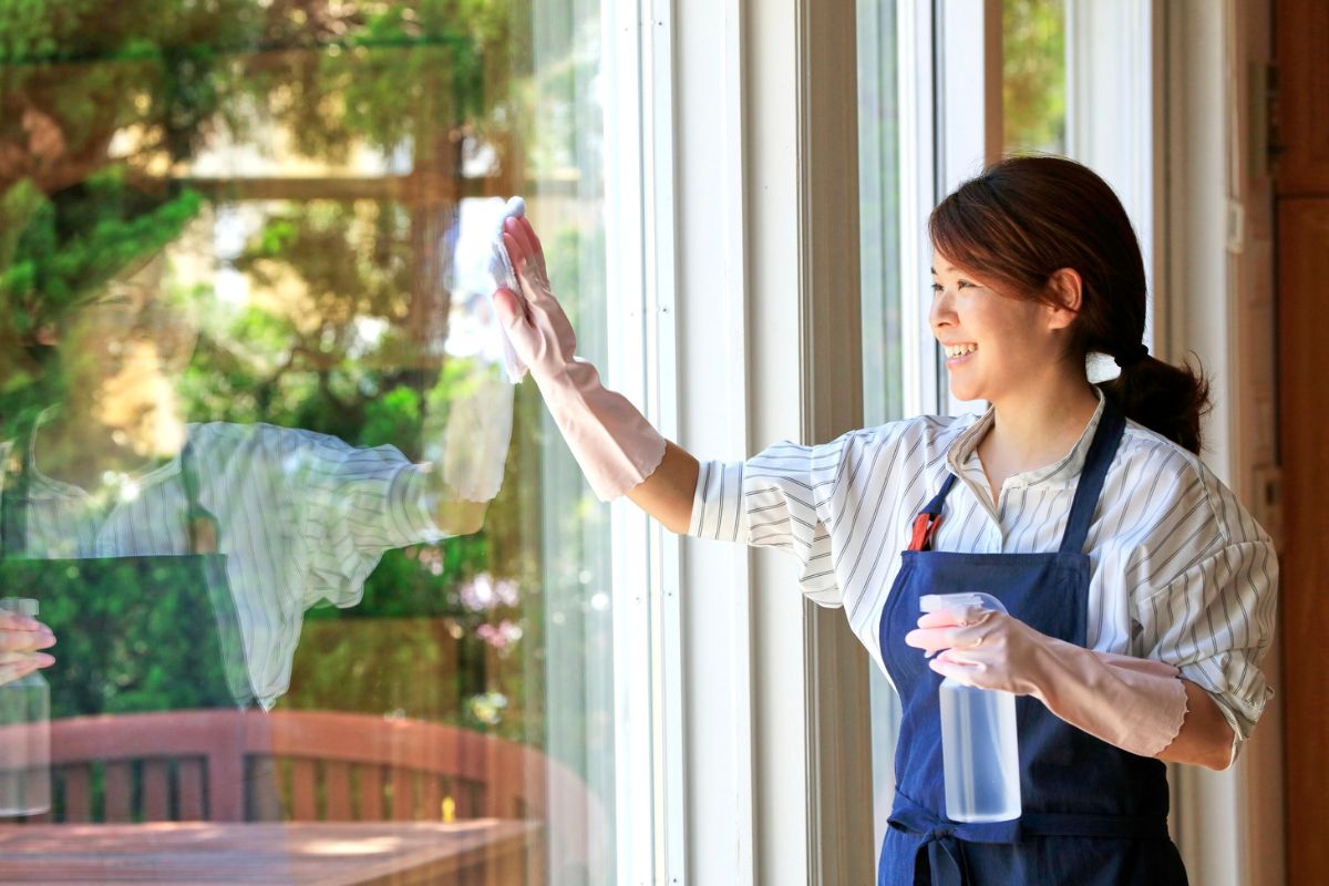 A woman wearing an apron is cleaning a window with a cloth, focused on making it shine.