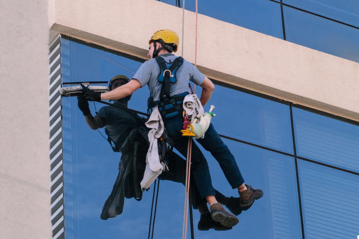 A man using a squeegee to clean windows on a tall building, with a clear blue sky in the background.