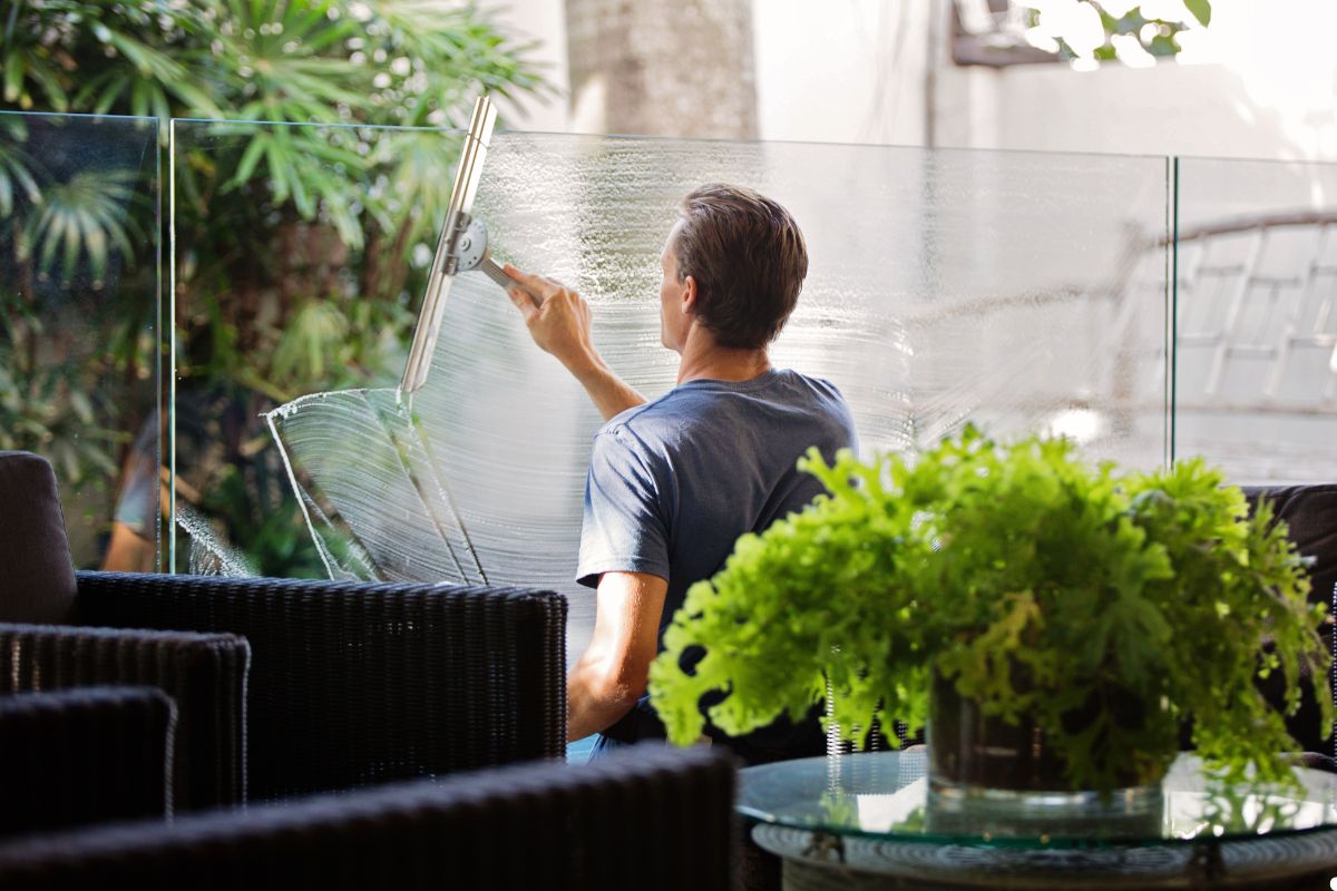 A man is using a cloth to clean glass panels on a patio, ensuring a clear view of the outdoor space.